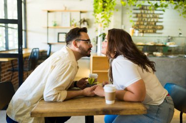 Bir kafede kahve içerken öpüşen ve el ele tutuşan güzel bir çiftin yan görüntüsü.