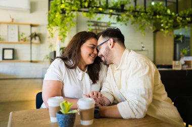 Bir kafede buluşurken el ele tutuşup romantik bir an yaşayan gülümseyen bir çift. 