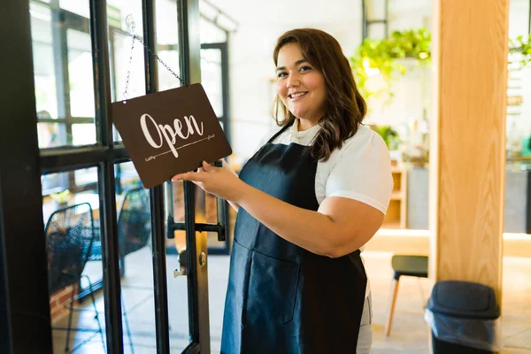 Portrait of a woman business owner smiling while putting an open sign on her restaurant or coffee shop