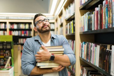 Kitapçıdan kitap alırken bir sürü kitap taşıyan heyecanlı genç adam mutlu görünüyor.