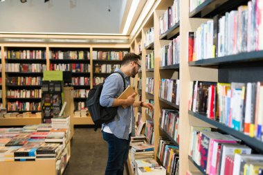 Üniversite öğrencisi kitaplığa bakıyor ve kitapçıdan akademik bir kitap almak istiyor.