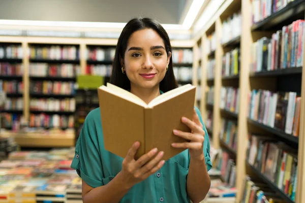 一位20多岁的漂亮女性读者在书店边看边买一本有趣的书的画像 — 图库照片