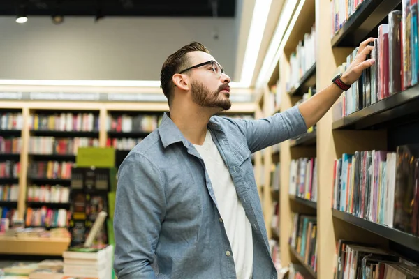 一个高加索人聪明男人在书店的书架上浏览的个人资料 — 图库照片