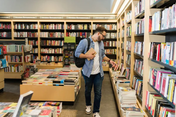 Smart man with a backpack shopping at the book shop and buying novels