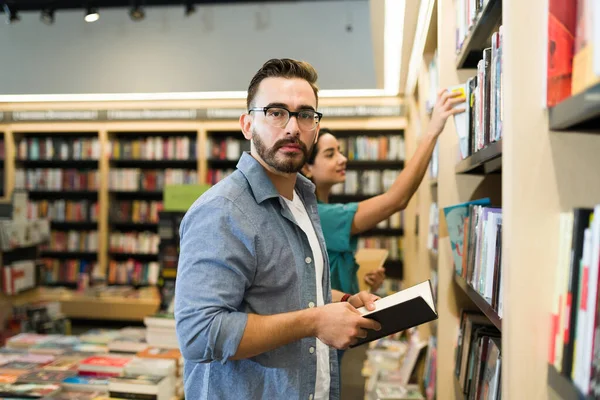 Caucasian man reader choosing an interesting novel while looking at the camera while buying books