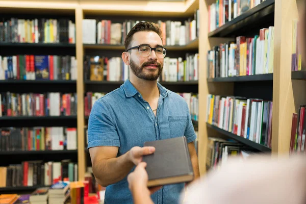 微笑的年轻人在书店寻求帮助 并得到了一本书的推荐 — 图库照片