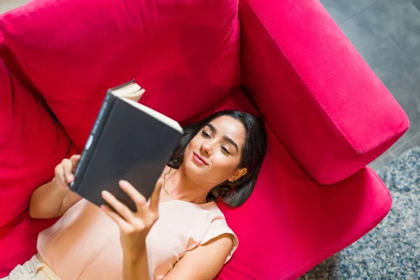 Lginç Bir Kitap Okurken Koltukta Dinlenen Rahat Genç Bir Kadının — Stok fotoğraf