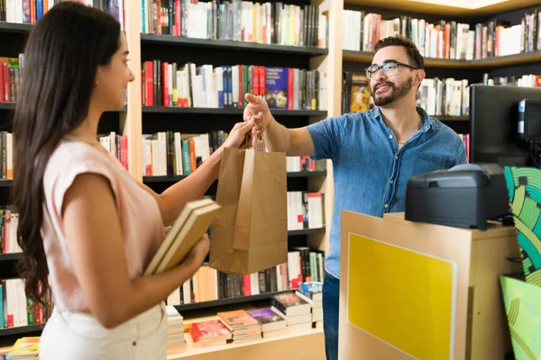 Caucasian happy worker giving the shopping bag to a customer reader buying books at the bookstore