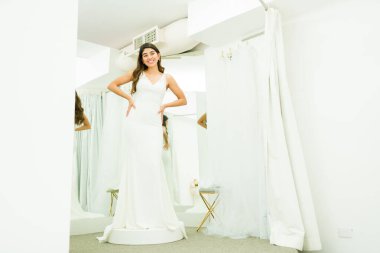 Gülümseyen genç bir kadın gelinlik alıyor ve soyunma odasında mutlu görünüyor.