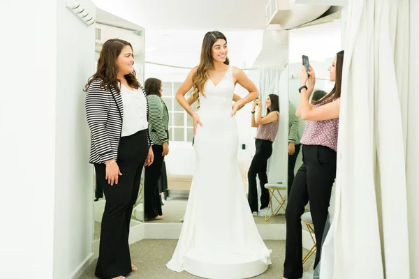 Друзья Подружки Невесты Фотографируют Латиноамериканку Примеряющую Красивое Свадебное Платье Гримерке — стоковое фото
