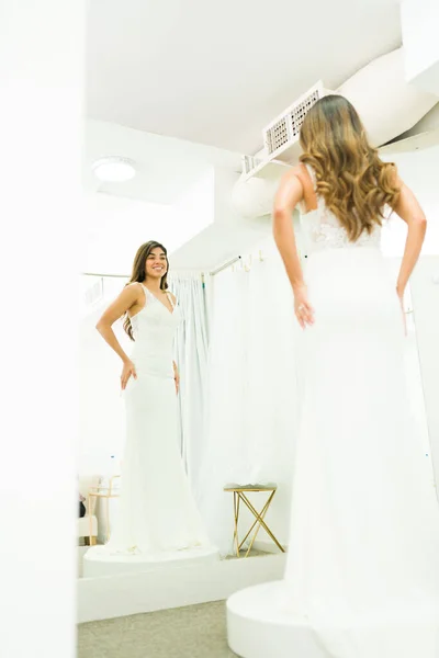 ウェディングドレスを買いながらドレッシングルームで鏡を見て後ろから見た幸せなラテン女性 — ストック写真