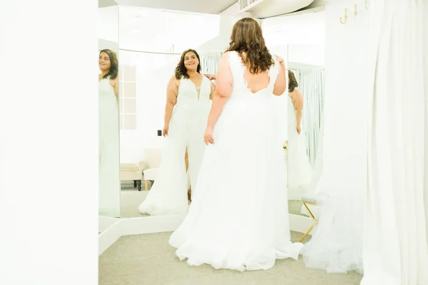 Rear view of a fat latin woman trying on a wedding dress in the dressing room of the bridal shop