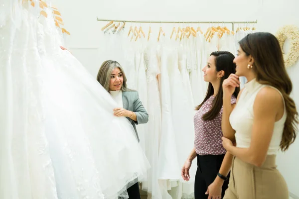 ブライダルショップで美しい若い女性にデザインのウェディングドレスを示すセールスマン — ストック写真