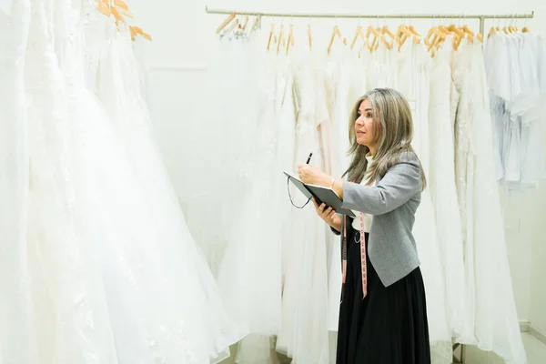 Sprzedawczyni Pięćdziesiątce Robi Inwentaryzację Sukienek Ślubnych Sklepie Ślubnym — Zdjęcie stockowe