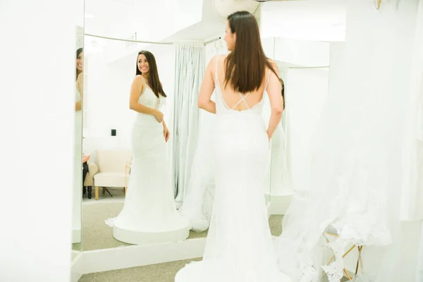 魅力的な幸せな女性を身に着けています結婚式のドレス鏡を見て ブライダルショップのドレッシングルームで笑顔 — ストック写真
