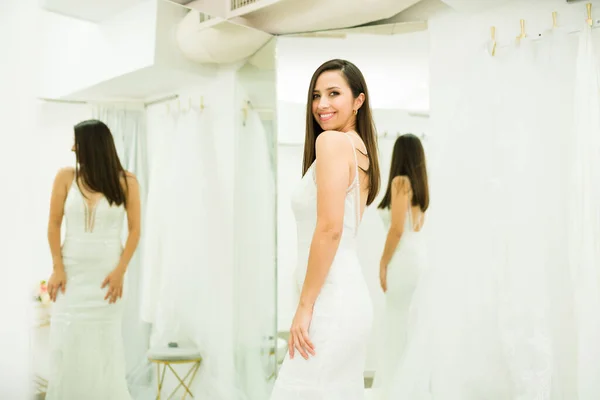 幸せなラテン女性にザブライダルショップ見てカメラと笑顔ながら身に着けている間に結婚式のドレス — ストック写真