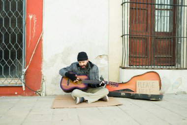 Zavallı evsiz dilenci sokakta para isterken şarkı söyleyip gitar çalıyor.