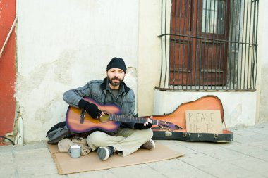 Yoksulluk içinde yaşayan bir dilenci şarkı söylemek ve sokakta para istemek için gitar çalar.