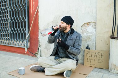 Alkolik, hasta, evsiz bir adam bir şişe alkol içiyor ve sokakta para istiyor. 