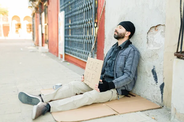 可悲的街头乞丐坐在地板上的纸板上 举着标牌 请求帮助购买食物 — 图库照片