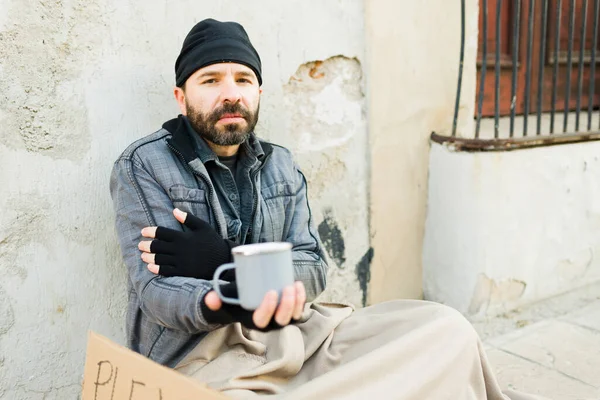 空腹悲しいホームレスの男作る目の接触中にカップを保持しながらお金を求めて寒さを感じる — ストック写真