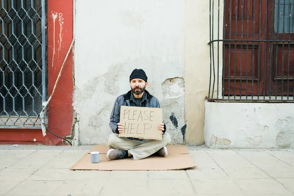 路上生活とカメラを見ている間に助けを求める段ボールの看板と貧困層のホームレスの男の肖像画 — ストック写真