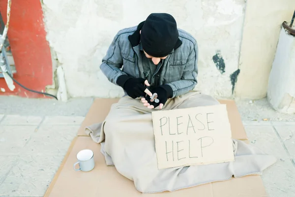 貧しいホームレスの男お願いのサインで段ボールに座っている間に食べ物を買うためにコインお金を数える — ストック写真