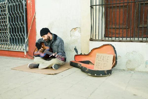 ホームレスの男がギターを弾いて歌を歌いながら 段ボールの看板付きの食べ物を求めている — ストック写真