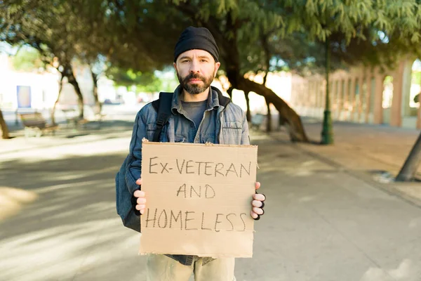 路上生活の元退役軍人とホームレスの男が段ボールの看板を持って助けを求めて苦労しながら — ストック写真