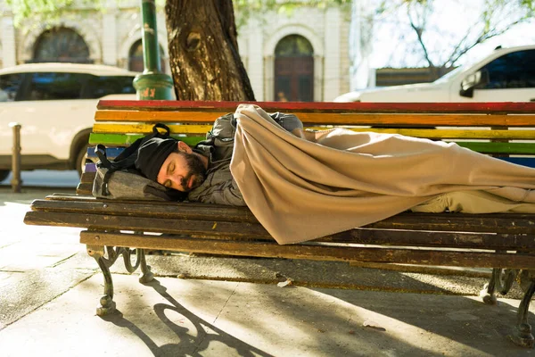 公園のベンチで一人で寝ている毛布で覆われた貧困の汚い冷たいホームレスの男 — ストック写真