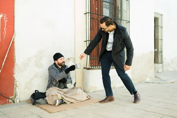 Caucasian man giving money for food to a homeless beggar sitting on cardboard on the street