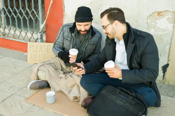 スマートフォンで写真や写真を見せる笑顔髭を生やしたホームレスの男性と一緒にコーヒーを飲みながら — ストック写真
