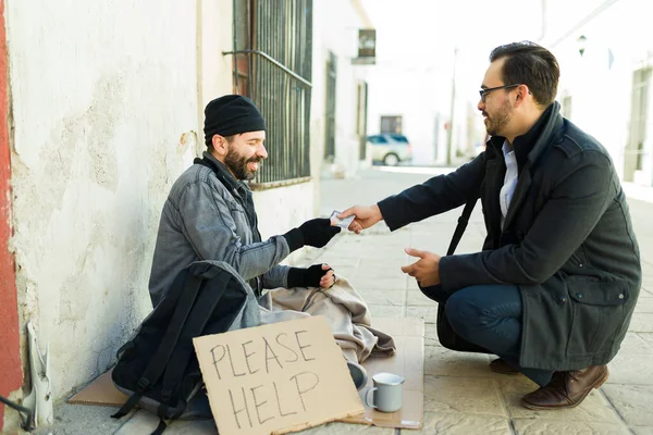 髭を生やした笑顔のホームレスの男に食べ物のためのお金を与える幸せな白人男性は段ボールのサインを助けてください — ストック写真