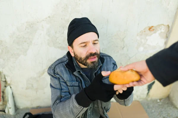 路上で男からパンを受け取った食べ物を見つけるのに苦労している悲しい空腹のホームレスの男 — ストック写真
