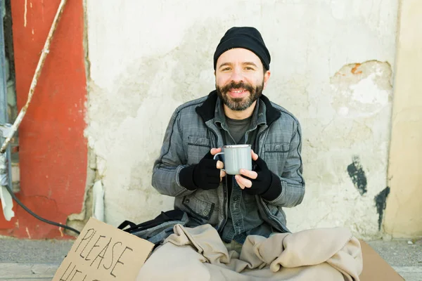 コーヒーを飲みながら笑顔で路上生活をしている幸せなホームレスの男性が段ボールサインをしてください — ストック写真