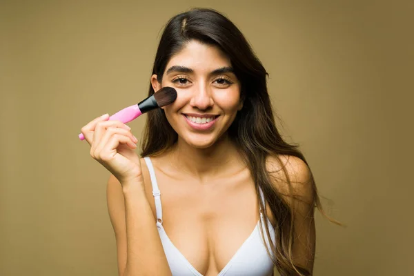 快乐美丽的年轻女性微笑着看着相机 一边用化妆品刷 一边在工作室前使用化妆品 — 图库照片