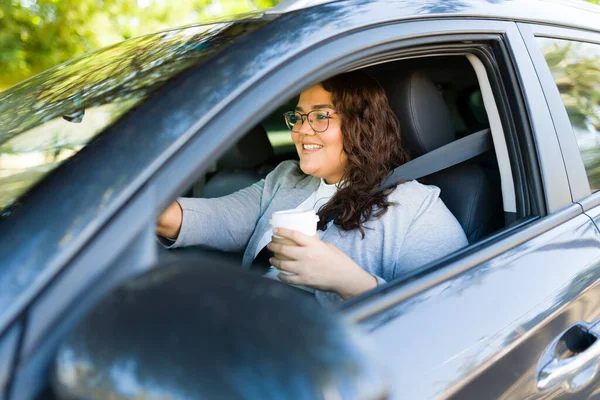 Cheerful beautiful obese woman smiling and drinking coffee to go in the morning while driving her car