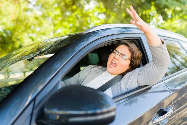 Angry big woman looking upset and with road rage while yelling to another driver while traveling by car