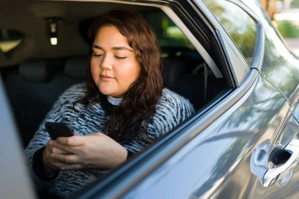 Hispanic obese woman and passenger texting on her smartphone while riding in the car after using a ride share app to travel