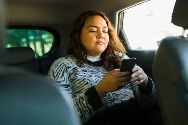 Beautiful latin obese woman and passenger texting on the smartphone while taking a trip on a ride share app