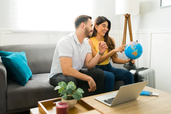 Cheerful couple at home choosing a country on the globle while planning to travel for vacations together