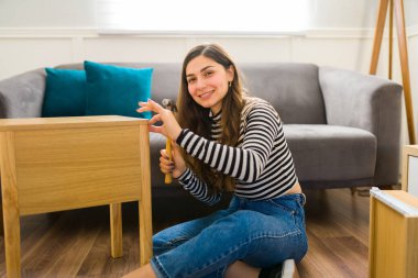 Beautiful happy woman looking at the camera while assembly a table and furniture in the living room clipart