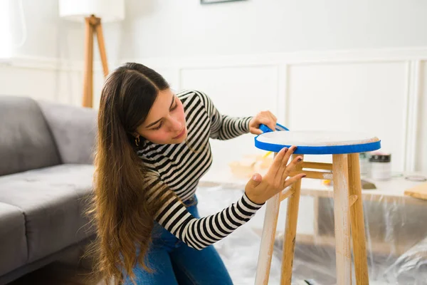 Beautiful woman with a furniture restoration business putting tape on a stool to start painting