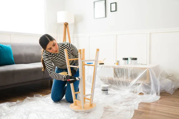 Hispanic woman painting furniture on a plastic sheet in the living room while doing restoration crafts