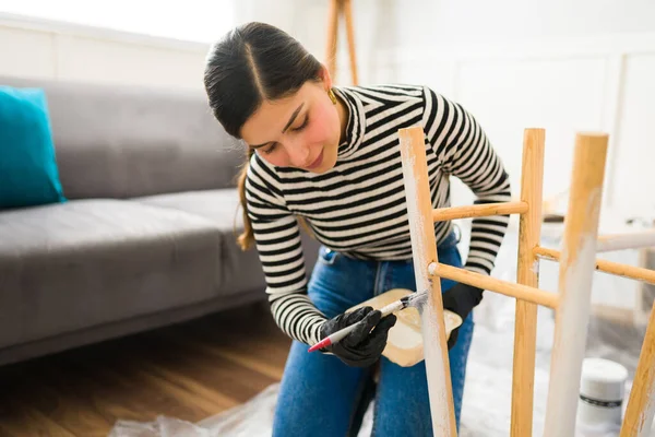Çekici bir kadın gülümsüyor ve mobilya boyarken dekorasyon sanatının zevkini çıkarıyor. 
