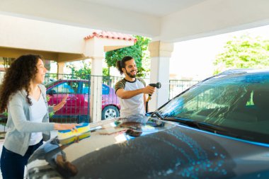 Arabasını sabunla yıkamak için kız arkadaşıyla birlikte hortum kullanan yakışıklı bir adam.