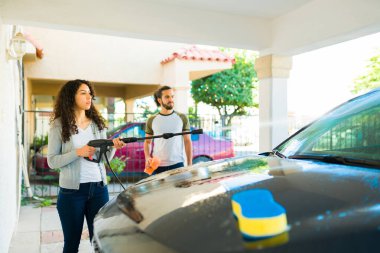 Arabasını erkek arkadaşıyla yıkamak için su tabancası kullanan çekici bir kadın. 