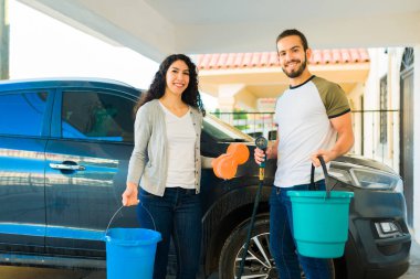 Çekici İspanyol çift evde arabalarını yıkamak için su ve sünger taşırken gülümsüyor.