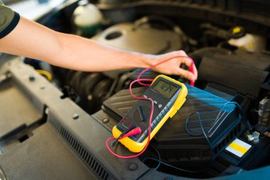 Araba motorunun aküsünü kontrol eden genç bir adamın ellerini kapat.