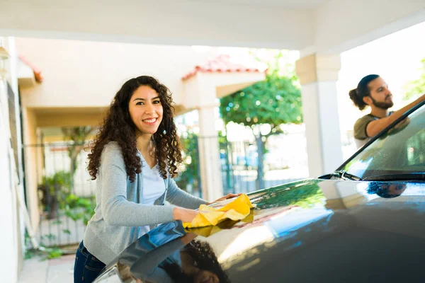 Beautiful young woman and her partner drying the ar after washing her car and looking happy